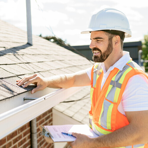 A man in a hard hat, holding a clipboard, standing on the steps of an old rundown house.
